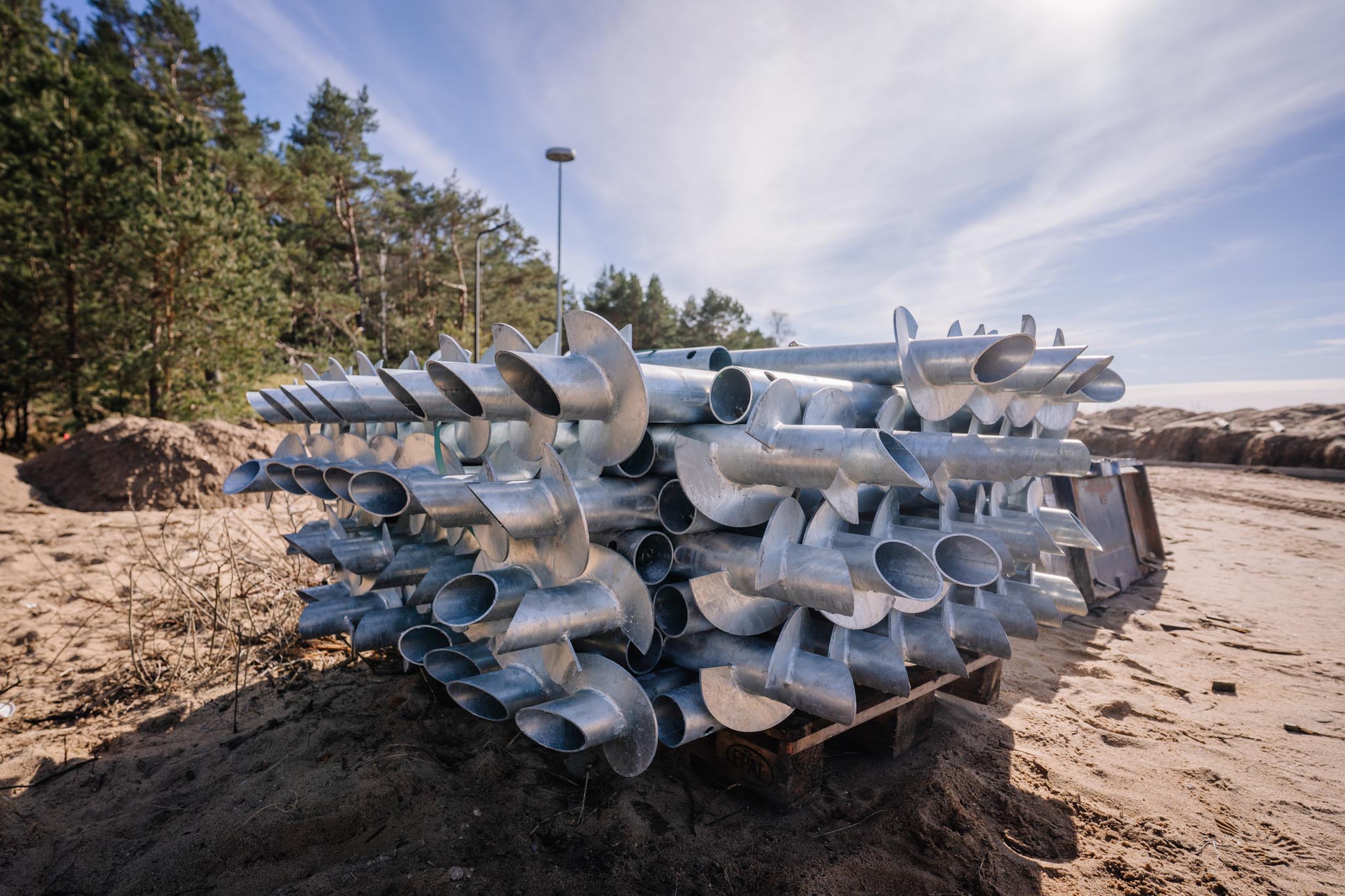 Pile of metal screw piles stacked on a pallet at a sandy constru